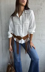 Camisa blanca de corte clásico con cuello camisero, mangas largas y detalle de bordado geométrico en el panel frontal superior. Confeccionada en tela liviana con textura.