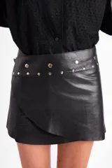 Minifalda de cuero de oveja color negro, con diseño envolvente y cierre mediante broches metálicos a presión en la cintura.
