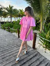 Vestido corto color beige de lino, con cuello mao, mangas cortas con volados, tablas en el canesú y falda escalonada con volantes.