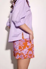 Camisa de lino texturado con diseño a rayas verticales rojas y blancas, cuello babero desmontable en color lila con volados y mangas cortas abullonadas.