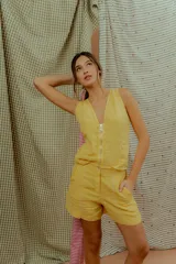 Chaleco de lino color amarillo, con escote en V, cierre frontal con tirador circular y costuras decorativas en contraste.
