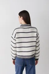 Cardigan de lana color bordó con cuello redondo, cierre frontal de botones y mangas largas. Presenta detalles de ribetes en contraste en cuello, puños y borde inferior, además de un bordado de raqueta de tenis en el pecho.