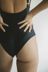 Malla de una pieza negra con escote en V profundo y tirantes finos. Presenta frunces sutiles bajo el busto para realzar la forma.