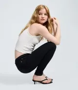 Pantalón skinny de tiro alto confeccionado en denim negro con elastano. Presenta cierre frontal con botón y cremallera, trabillas para cinturón y bolsillos funcionales tanto en el frente como en la parte posterior.
