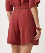 Short suelto color bordó con pinzas frontales, bolsillos laterales y cierre con cremallera y botón. Incluye cinturón fino de rafia con hebilla metálica.