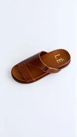 Sandalias de cuero color marrón con diseño asimétrico de tiras y plantilla anatómica. Tienen ajuste lateral con velcro y suela plana.