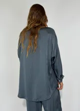 Camisa blanca de satén con cuello clásico, cierre frontal con botones y mangas largas.