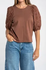 Remera de algodón color rosado con mangas cortas abullonadas de broderie con diseño floral calado. Presenta cuello redondo y costura vertical central en el frente.