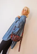 Bandolera de cuero color rojo con detalles en negro, con correa regulable y cierre superior con cremallera.