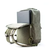Mochila matera y porta notebook en tela canvas de color marrón, con diseño funcional que incluye bolsillo frontal con cierre, correas ajustables, manija superior y detalles de tiras de lona con hebillas metálicas.