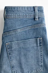 Jean de denim de algodón con leve stretch, tiro alto y piernas amplias de corte holgado. Presenta bolsillos traseros de parche, cierre con botón y pliegues en la parte delantera y trasera.