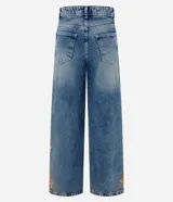 Pantalón wide leg de jean azul con bordado floral aplicado en los laterales. Posee cintura mediana con trabillas, cierre frontal con botón y cremallera, y bolsillos funcionales.