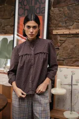 Camisa de broderie color chocolate, con cuello alto con volados, cierre frontal de botones y mangas largas con volumen.