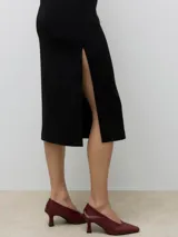 Vestido midi negro, ajustado al cuerpo, con escote cuadrado y tirantes finos. Presenta un tajo lateral en la falda.