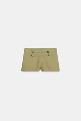 Shorts mini de tiro alto color verde militar, con detalle de botones metálicos y aplicaciones en la parte delantera.