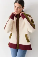 Campera de tejido de punto con cierre frontal, cuello alto y diseño color block en tonos marrón, rosa y rojo. Presenta detalles de trenzas en las mangas y puños y ruedo acanalados.