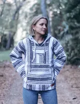 Buzo estilo mexicano con capucha, tejido en hilo grueso a rayas horizontales blancas y negras, con bolsillo tipo canguro y cordones ajustables en el cuello.
