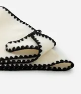 Bufanda de punto color crema con bordes decorados con pespunte en hilo negro. Presenta un diseño rectangular y etiqueta de la marca Accessories.