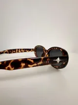 Lentes de sol con armazón ovalado de color negro y cristales tonalidad marrón. Presentan un detalle metálico en forma de estrella en las patillas.