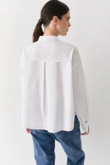 Camisa de corte recto y holgado, color blanco, con cuello mao y cierre frontal de botones. Presenta costuras a la vista en color contrastante, bolsillo lateral tipo parche y puños anchos con detalle bordado.