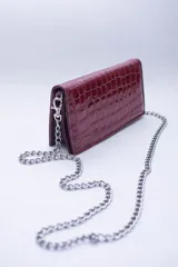Cartera de mano color borgoña con textura símil cocodrilo y cadena metálica plateada removible.