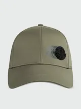Gorra de béisbol Moncler color verde oliva, con diseño de seis paneles y visera curva. Presenta un parche circular negro con el logo de la marca en relieve y un efecto visual de movimiento impreso debajo.