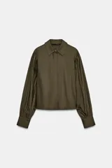 Camisa de popelín color verde militar, con cuello solapa, mangas largas abullonadas terminadas en puño, bajo recto y cierre frontal con botones ocultos por solapa.