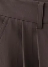 Pantalón balloon de tiro medio color marrón oscuro, con diseño de pinzas, trabillas y bolsillos laterales. Cuenta con cierre de gancho y cremallera.