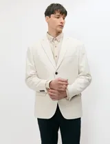 Blazer de medio forro color beige, confeccionado en mezcla de algodón y lino. Presenta una silueta estructurada con solapas de muesca, cierre frontal de un botón y bolsillos con solapa.