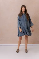 Vestido camisero corto de denim liviano azul con efecto desgastado, de corte oversize, con cuello camisero, botonadura frontal, bolsillo plaqué en el pecho, mangas largas y volado fruncido en el ruedo.