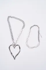 Set de dos collares plateados. Uno de ellos presenta una cadena de eslabones combinada con perlas irregulares y un dije grande en forma de corazón. El otro collar es una gargantilla de perlas irregulares con una sección de cadena de eslabones y cierre ajustable.