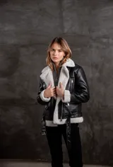 Campera tipo gamulán de eco cuero negro con interior y solapas de corderito sintético en color crudo. Presenta cierre frontal, bolsillos laterales con cierre y cinturón ajustable en la cintura.