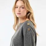 Sweater de punto color gris, de corte recto y largo a la cintura. Presenta cuello redondo y detalle de botones decorativos dorados en uno de los hombros.