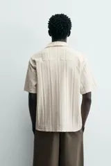 Polo de hombre color crema, de tejido texturado con rayas verticales en relieve, corte relajado, cuello bowling y cierre frontal parcial con botones.