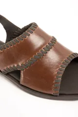 Sandalia plana de cuero marrón, con tiras cruzadas anchas en el empeine decoradas con costuras pespunteadas en contraste y tira con hebilla ajustable al tobillo.