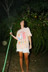 Remera oversize color beige con estampa frontal colorida con motivos de verano, incluyendo texto 'TA'CALOR' y 'PICA X PETRICHOR'.