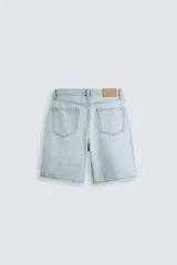 Bermuda de denim de algodón, color verde claro lavado, de corte recto y tiro medio. Presenta cinco bolsillos y cierre frontal con cremallera y botón.
