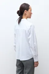 Camisa blanca de manga larga con cuello alto y volados en el cuello y puños.