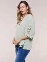 Blusa verde de algodón, marca Erika, con cuello redondo, escote en V y botones frontales. Cuenta con mangas cortas decoradas con botones laterales y diseño de corte holgado.