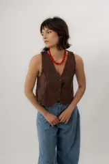 Chaleco de denim azul con cuello en V, cierre frontal con botones metálicos y pespuntes en contraste.