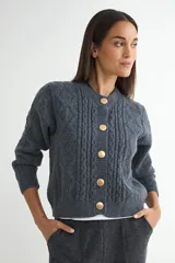 Cardigan de punto gris con textura trenzada, cuello redondo y cierre frontal con botones dorados grandes. Posee mangas largas con puños ajustados y un corte recto.
