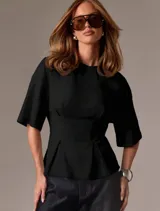 Remera negra de diseño estructurado con silueta entallada, mangas amplias y detalles de pinzas en la cintura que realzan la figura.