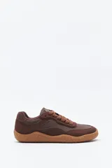 Zapatilla de estilo barefoot color marrón, confeccionada con una combinación de gamuza y materiales sintéticos. Presenta un diseño de perfil bajo con suela de goma flexible en color caramelo que incluye el logo de la marca grabado en el lateral.