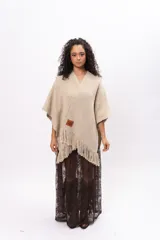 Ruana de tejido de punto en color arena, con diseño cruzado, escote en V y terminaciones con flecos en el ruedo. Incluye un parche de cuero con la marca Pura Lana en la parte frontal.
