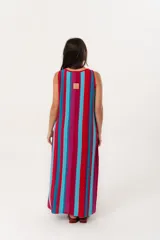 Vestido largo tejido de punto con diseño de rayas verticales en colores vibrantes, escote bote y mangas sisa. Presenta tajos laterales en el ruedo que aportan movimiento.