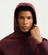 Campera deportiva Get Over de hombre, color bordó, con capucha ajustable, cierre frontal y bolsillos con cremallera. Confeccionada en tejido técnico resistente al agua.