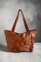 Cartera tipo tote de cuero natural color suela, con diseño envolvente, asas largas de hombro, bolsillo exterior y llavero metálico decorativo con logo.