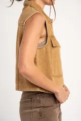 Chaleco de jean tostado con efecto lavado, cuello camisero, cierre frontal con botones metálicos y bolsillos delanteros con solapa. Diseño sin mangas y corte al cuerpo.