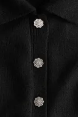 Saco de punto de manga corta con cuello camisero, cierre frontal con botones decorados con strass y terminaciones acanaladas en mangas y ruedo.