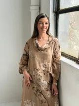 Vestido largo de lino color camel con estampado floral en tonos marrón y crudo, cuello drapeado y mangas largas holgadas.